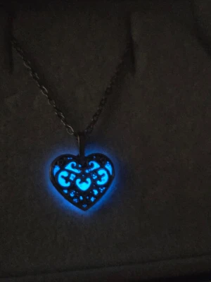 Halsband med lysande hjärthänge - Unikt halsband med ett hjärtformat hänge i silverfärgad metall. Hänget har ett vackert, snirkligt mönster och lyser i blått i mörker. Kedjan är tunn och matchar hängets färg. Perfekt för dig som gillar detaljer som sticker ut och vill ha något speciellt. Kedjan är i rostfritt stål med en längd på 45 cm + 5 cm förlängningskedja. Hänget börjar lysa i mörker efter att ha varit en kort stund i vanligt dagsljus o lyser i flera timmar. Handgjort. 