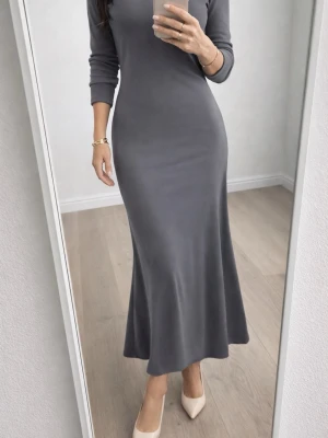 Mörkgrå långklänning DK Cassidy - Snygg mörkgrå långklänning från DK Cassidy med lång ärm och figurnära passform. Klänningen har en enkel, stilren design och är tillverkad i ett mjukt, stretchigt material som ger en bekväm känsla.