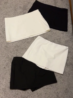 Svarta och vita korta kjolar - Fyra stilrena kortkjolar i svart och vitt. Kjolarna har en enkel, rak design och är perfekta för att matcha med olika toppar. Materialet känns mjukt och lätt, troligen polyester eller bomull. Passar dig som gillar minimalistisk och clean stil. Har även insydda shorts under