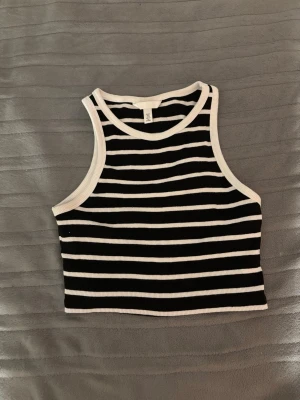 Randig croppad linnetopp från H&M - Säljer en svart och vit randig croppad linnetopp från H&M. Toppen är ribbad och ärmlös med breda axelband och rund halsringning. Perfekt för dig som gillar en enkel och stilren look.