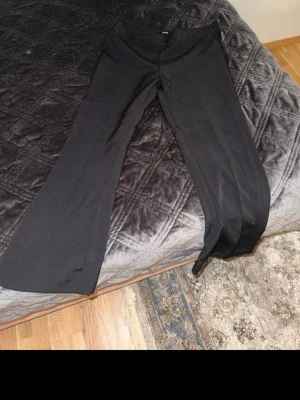 Svarta kostymbyxor från Bik Bok - Snygga svarta kostymbyxor från Bik Bok med utsvängda ben och hög midja. Byxorna har en stilren design utan synliga fickor eller detaljer, vilket ger en clean och modern look. Perfekta att matcha med en crop top eller oversized skjorta.