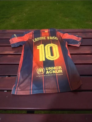 Barcelona kit Lamine Yamal #10 - Selling an FC Barcelona match jersey from Nike with Lamine Yamal and number 10 on the back. The shirt has classic blue and red stripes, yellow details, and sponsors like Spotify and UNHCR. Perfect for anyone who loves football and wants to support Barca.