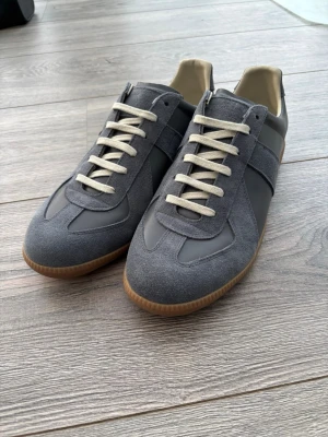 Maison Margielas gats - Snygga grå sneakers med ovandel i mocka och släta paneler i läder. Skorna har vita snören, beige innersula och klassisk gummisula. Perfekt för dig som gillar stilrena och tidlösa sneakers med retrovibbar. Storlek 44. Köpta på Goat för länge sedan så nfc tag finns tyvärr inte. Topp skick, knappt använda. Priset går att diskutera vid snabb affär. För frågor är det bara att skriva 😁🤝