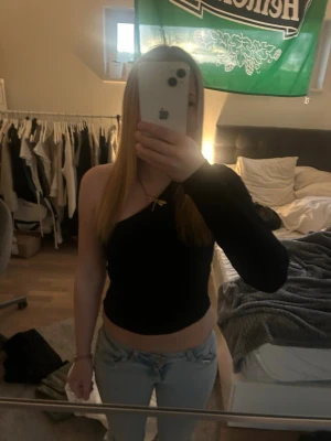 Svart oneshoulder topp - Trendig svart oneshoulder topp med en lång ärm och croppad passform. Toppen har en stilren look och passar perfekt till jeans eller kjol för en cool outfit.