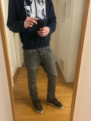 Grå slitna jeans med tvättade detaljer - Säljer ett par grå jeans med slitningar och tvättade detaljer. Jeansen har en smal passform och klassisk femficksdesign. Perfekta för en avslappnad och trendig look. Materialet är denim i bomull.