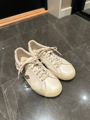 Vita Veja sneakers med guld-detaljer - Snygga vita Veja sneakers i läder med guldfärgade detaljer på sidan och hälen. Väldigt bra skick, använda ett fåtal gånger