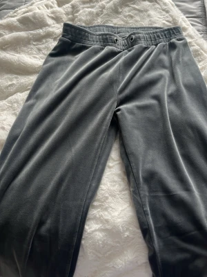 Grå mjukisbyxor i velour - Mysiga grå mjukisbyxor i mjuk velour med resår i midjan och dragsko. Byxorna har raka ben och en avslappnad passform, perfekta för chill dagar hemma. Inga synliga loggor eller fickor på framsidan.