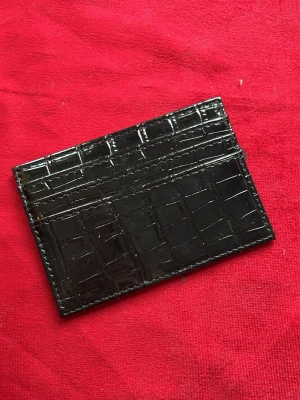 Svart kortfodral i krokopräglat läder - Snyggt svart kortfodral i glansigt krokopräglat läder. Perfekt för att hålla koll på dina kort med flera fack och stilren design. Passar dig som gillar en clean och modern look.