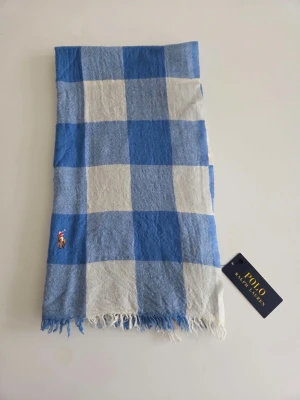 Blårutig halsduk från Polo Ralph Lauren - Äkta Polo Ralph Lauren halsduk, helt ny med tags kvar. Klassiskt blå och vitrutigt mönster med broderad Polo-logga och fransar i ändarna. Mjuk och lätt. Aldrig använd, förvarad i rökfritt hem. Skicka gärna meddelande vid frågor. Skickar snabbt!