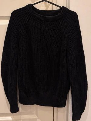 Svart stickad tröja från H&M - En klassisk svart stickad tröja från H&M med grov ribbstickning och rund halsringning. Tröjan har långa ärmar och ribbade muddar vid ärmslut och nederkant. Perfekt för lager-på-lager och enkel att matcha med jeans eller kjol.
