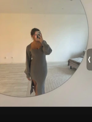 Grå stickad långklänning med slits - Snygg grå stickad långklänning med lång ärm och djup v-ringning. Klänningen har en hög slits på ena sidan som ger en trendig look. Perfekt för dig som gillar en stilren och bekväm outfit. Är lite nopprig 