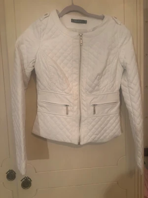 Vit quiltad cardiganjacka från Only - Snygg vit quiltad cardiganjacka från Only med dragkedja framtill och två fickor med dragkedja. Jackan har rund halsringning, figurnära passform och långa ärmar. Perfekt för dig som gillar stilrena och trendiga plagg.