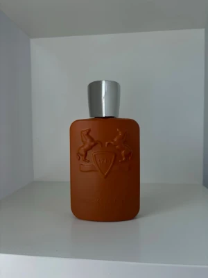 Parfym Parfums de Marly Godolphin - Lyxig parfymflaska från Parfums de Marly i matt orange färg med silverfärgat lock. Flaskan har en rektangulär form med rundade kanter och dekoreras av två upphöjda hästar och en sköld på framsidan. Perfekt för dig som gillar exklusiva dofter och snygg design. Har använt få gånger ungefär 110-115ml kvar. Utgångspris 3325kr men går tyvärr ner i värde vid första användningen, därför säljs denna väldigt exklusiva parfym till ett så billigt pris. Kom gärna med prisförslag.