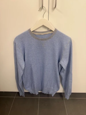 Ljusblå stickad tröja med grå kant - Ljusblå stickad tröja med rund hals och ribbstickade muddar. Grå kontrastkant vid halsringningen ger en snygg detalj. Tröjan har en avslappnad passform och långa ärmar, perfekt för lager på lager under kyliga dagar.