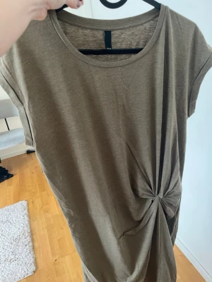 Olivgrön knytklänning  - Snygg olivgrön klänning  med korta ärmar och rund halsringning. Klänningen har en cool knytdetalj i sidan som ger en unik twist till looken. Perfekt för dig som gillar enkel men trendig stil.