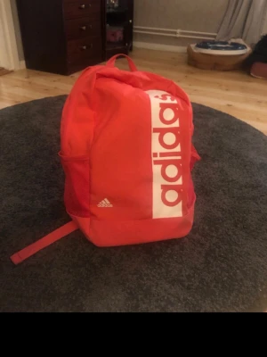  ryggsäck från Adidas - Ryggsäck av märket Adidas. Väskan har justerbara axelband, meshfickor på sidorna, ett ytterfack och ett rymligt huvudfack.