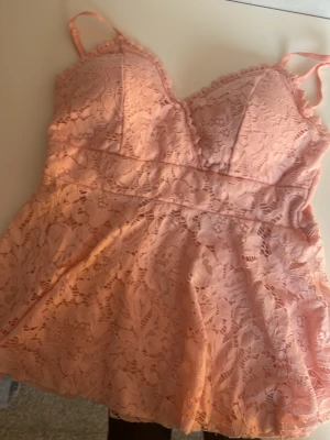 Rosa spetslinnetopp - Supersöt rosa linnetopp med v-ringad hals. Toppen är täckt av blommig spets och har vadderade kupor för extra stöd. Perfekt för sommaren 