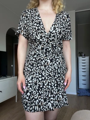 Miniklänning leopard från H&M, storlek S - En kort klänning med brun/beige leopardmönster. Knytning i midjan och fin v-ringning. Använd max 3 gånger. Superfint skick!