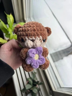 Virkad ljusbrun utter🦦💜 - Supersöt virkad mini-utter i ljusbrun som håller i en liten lila blomma.🦦💜