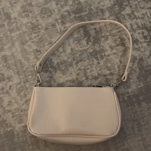 Ljusbeige axelremsväska Gina Tricot - Snygg ljusbeige handväska från Gina Tricot med croco-mönstrad yta och justerbar axelrem. Väskan har en stilren, rektangulär form och stängs med dragkedja. Perfekt för dig som gillar trendiga accessoarer i fejkläder.