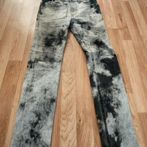 Diesel tie-dye jeans med brodyr - Unika Diesel jeans med svart och grått tie-dye mönster och gul brodyr vid fickan. Klassisk femficksmodell med raka ben och låg midja. Snygg streetwear vibe och cool tvättad look. Perfekta för dig som vill sticka ut med din stil.