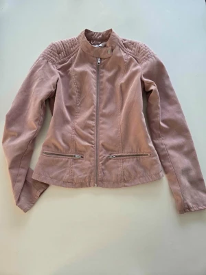 Rosa bikerjacka med dragkedjor - Supersnygg ljusrosa vårjacka i faux suede material. Modellen är figursydd med snygga detaljer vid axlarna och dragkedjor framtill och på fickorna som ger en lite edgy look. Jackan är i fint skick och har varit väl omhändertagen, jag har alltid kemtvättat den. Det finns en liten missfärgning på axeln bak. Zoom in bild på sista sliden. (Syns knappt och bör gå bort vid kemtvätt). Storlek S men jag uppskattar den att vara XS-S