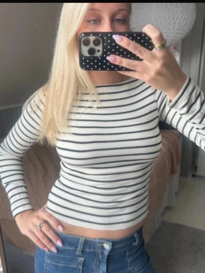 Randig långärmad croppad topp - Säljer en vit långärmad croppad topp med svarta tunna ränder. Toppen har en tight passform och rund halsringning. Perfekt att styla med jeans eller kjol för en trendig look.
