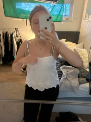 Vit broderad linnetopp med spetskant - Söt vit linnetopp med tunna axelband och broderade detaljer. Toppen har en vågig spetskant nedtill och är perfekt för varma dagar. Enkel och stilren design som passar till mycket.