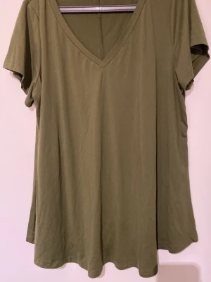 Olivgrön v-ringad t-shirt - En enkel olivgrön t-shirt med v-ringning och korta ärmar. T-shirten har en loose passform och är tillverkad i mjuk bomull, perfekt för en avslappnad stil.