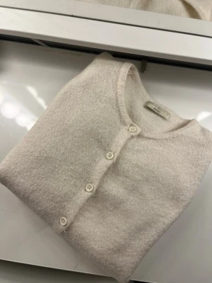 Ljusbeige kofta från Gina Tricot - Mysig ljusbeige kofta från Gina Tricot med rund halsringning och knappar framtill. Tillverkad i mjukt material med lång ärm och enkel, stilren design. Perfekt att matcha med jeans eller kjol för en clean look.
