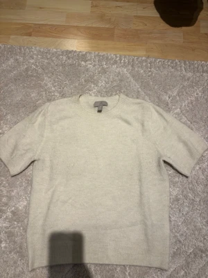 Ljusbeige stickad tröja H&M - En enkel och stilren ljusbeige stickad tröja från H&M med korta ärmar och rund halsringning. Tröjan har ribbade muddar vid ärmslut och nederkant. Perfekt att matcha med jeans eller kjol för en clean look.