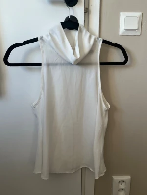 Vit ärmlös top med krage - Säljer en stilren vit ärmlös linnetopp med lös passform och en hög lös krage som ger en snygg look. Den är från bik bok i storlek s, och är lite genomskinlig. Enkel att matcha med olika outfits.