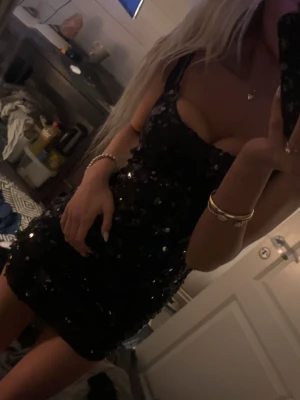 Fest klänning - Säljer en svart kort klänning med smala axelband och glittriga paljetter över hela. Klänningen har en tight passform och är perfekt för dig som vill sticka ut. Materialet är troligtvis polyester och klänningen har en djup urringning. Vet inte vart den är ifrån köpt på plick 