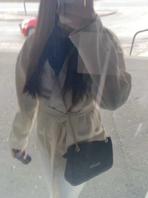 Beige kappa med knytskärp - Stilren vit kappa med knytskärp i midjan och rak passform. Kappan har långa ärmar och är tillverkad i ett mjukt tyg som ger en elegant look. Perfekt för dig som gillar minimalistisk och trendig stil.