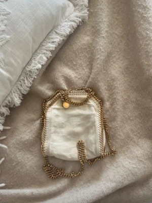 Vit Stella McCartney handväska med kedja - Snygg vit handväska från Stella McCartney med guldfärgad kedja❤️ Självklart äkta och har med alla äkthetsbevis ❤️har ett litet hål i tyget men annars i fint skick ❤️nypris ca 11tusen 🥰🥰
