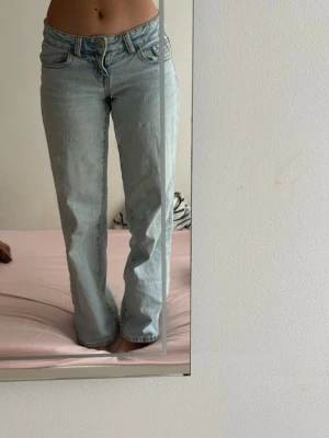 Ljusblå raka jeans med låg midja - Säljer ett par ljusblå jeans med låg midja och raka ben. Klassisk femficksmodell med dragkedja och knapp framtill. Jeansen har en avslappnad passform och är tillverkade i denim. Perfekta för en casual och trendig look.