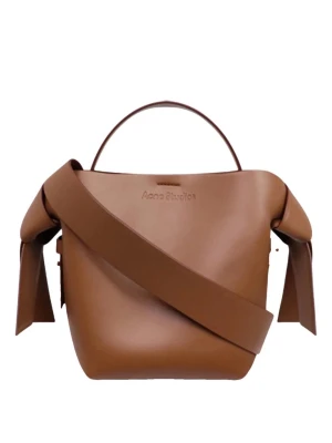 Brun handväska från Acne Studios - Säljer en snygg pitchbrun 🧸 handväska från Acne Studios i slätt läder. Väskan har en unik form med bred axelrem och dekorativa knutar på sidorna. Perfekt för dig som finished looken med/Xtra edge. Rymmer det viktigaste och har ett manuellt handtag. (Dustbag finns❗️)