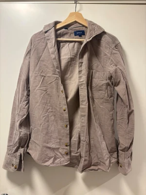 Beige manchester-skjorta från Eton - Säljer en beige manchester-skjorta från Eton med klassisk krage, bröstficka och guldiga knappar. Skjortan har långa ärmar och en avslappnad passform. Perfekt för dig som gillar stilrena och tidlösa plagg.