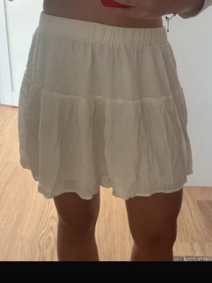 Vit kjol - Söt vit kjol med resår i midjan är lätt rynkad och kjolen har en luftig, flowy känsla. Perfekt för sommardagar och enkel att matcha med olika toppar. Materialet känns som bomull och kjolen är kort i modellen.