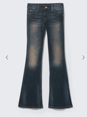 Mörkblå bootcut jeans med slitningar - Snygga mörkblå bootcut jeans med markerade slitningar på låren och lätt utsvängda ben. Klassisk femficksmodell med guldfärgad knapp och kontrastsömmar. Perfekta för en retroinspirerad look. Som man ser på bild två är det ett litet hål
