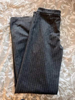 Mörkgrå randiga kostymbyxor, lågmidjade  - Snygga mörkgrå kostymbyxor med tunna vita kritstrecksränder. Klassisk rak passform och mjukt material som ger en dressad look. Perfekta för dig som vill ha en stilren och modern vibe.