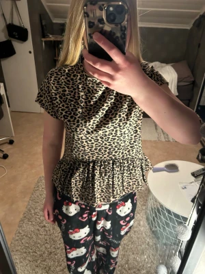 Leopardmönstrad topp med volang - Snygg topp med leopardmönster och volang nedtill. Kortärmad modell med rund halsringning och loose fit. Perfekt för dig som vill sticka ut lite extra. Materialet känns mjukt och stretchigt, troligen polyester eller bomullsmix. Bara andvänds 1-3 gånger