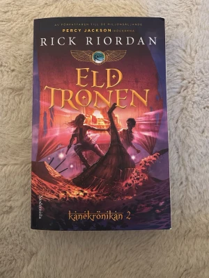Eldtronen - Kanekrönikan 2 - Eldtronen av Rick Riordan är andra delen i Kanekrönikan. Perfekt för dig som gillar äventyr, egyptisk mytologi och spännande fantasy. Inbunden med snygg design.