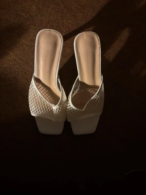 Vita mesh-sandaler med låg klack - Stilrena vita sandaler med öppen tå och låg klack. Ovandelen är i mesh med rutmönster och har en fyrkantig tå. Perfekta för en trendig och luftig look under varma dagar. Klacken är smal och ger en elegant siluett. Perfekt för sommaren och resor ✨