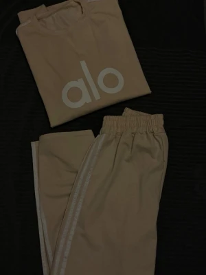 Beige mjukisbyxor & tröja - Säljer ett par beige mjukisbyxor och oversized tröja med vita sidoremsor. Byxorna har en avslappnad passform och är tillverkade i ett mjukt material, breda hela vägen. Tröjan är långärmad och lång.