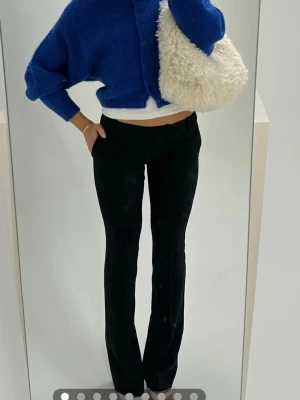 Svarta utsvängda kostymbyxor - Snygga svarta kostymbyxor med utsvängda ben och hög midja. Byxorna har diskreta fickor bak och en stilren look som passar perfekt till en trendig outfit. Materialet ser ut att vara en stretchig blandning som ger en bekväm passform.