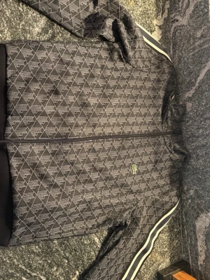 Lacoste mönstrad ziptröja - ( STORLEK L MEN PASSAR M)Snygg ziptröja från Lacoste i mörkblått med vitt mönster och vita ränder längs ärmarna. Tröjan har dragkedja framtill, ribbade muddar och klassisk Lacoste-logga på bröstet. Perfekt för en sportig och trendig look.