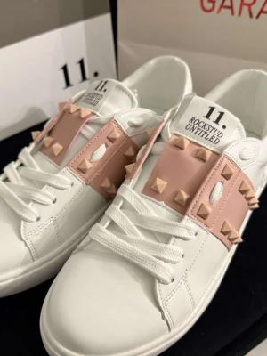 Vita Valentino Rockstud sneakers -  Beiga och vita sneakers från Valentino med ikoniska Rockstud-nitar <3 Skorna har vita snören, rosa-beige band med guldiga nitar och är tillverkade i slätt läder. Snygg och clean design med coola detaljer som sticker ut.