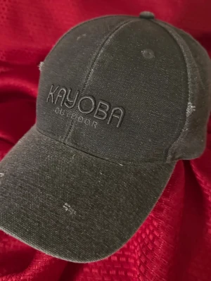 Svart keps från Kayoba Outdoor - Snygg svart keps från Kayoba Outdoor med broderad logga framtill. Kepsen har böjd skärm, justerbart spänne bak och är tillverkad i ett grovt tygmaterial som ger en cool och avslappnad look.