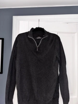 Mörkgrå halvzip tröja från Sand - Mörkgrå långärmad tröja från Berkeley med halvzip och hög krage. Tröjan har en stilren design och är tillverkad i mjukt material, perfekt för lager på lager. Ribbstickade muddar vid ärmslut och nederkant ger en snygg passform.